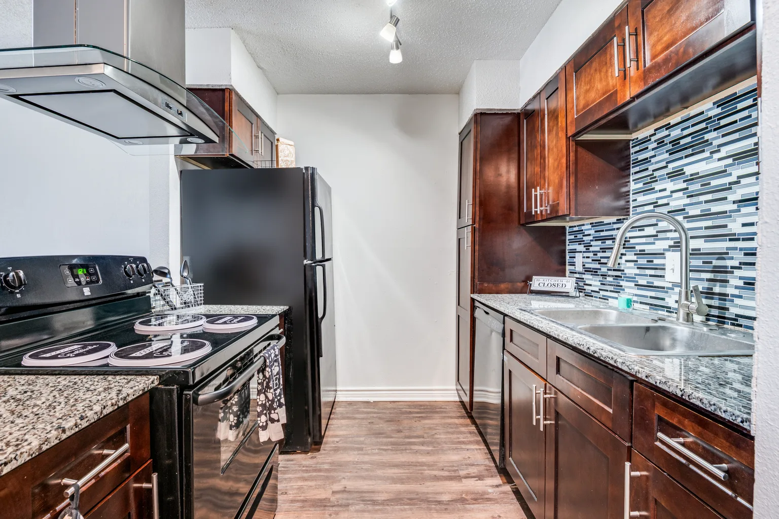 A kitchen with dark cabinets, a glass mosaic backsplash and granite counters.