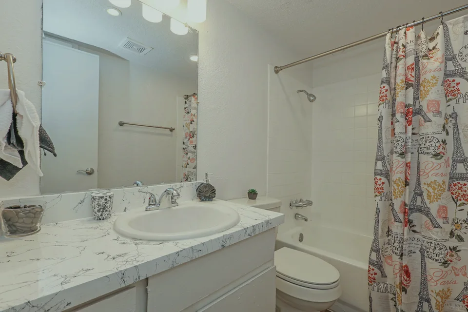 A bathroom with a white vanity, a light stone counter and the tub behind a curtain.