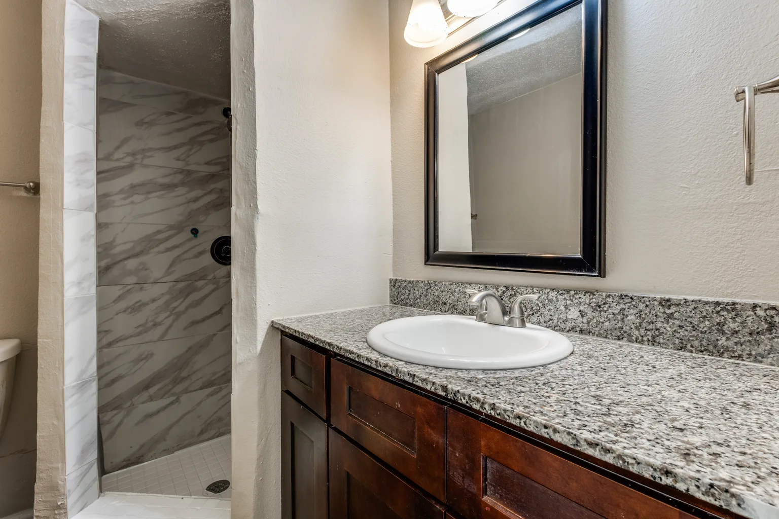 A bathroom with a tiled shower and a dark vanity under a framed mirror.