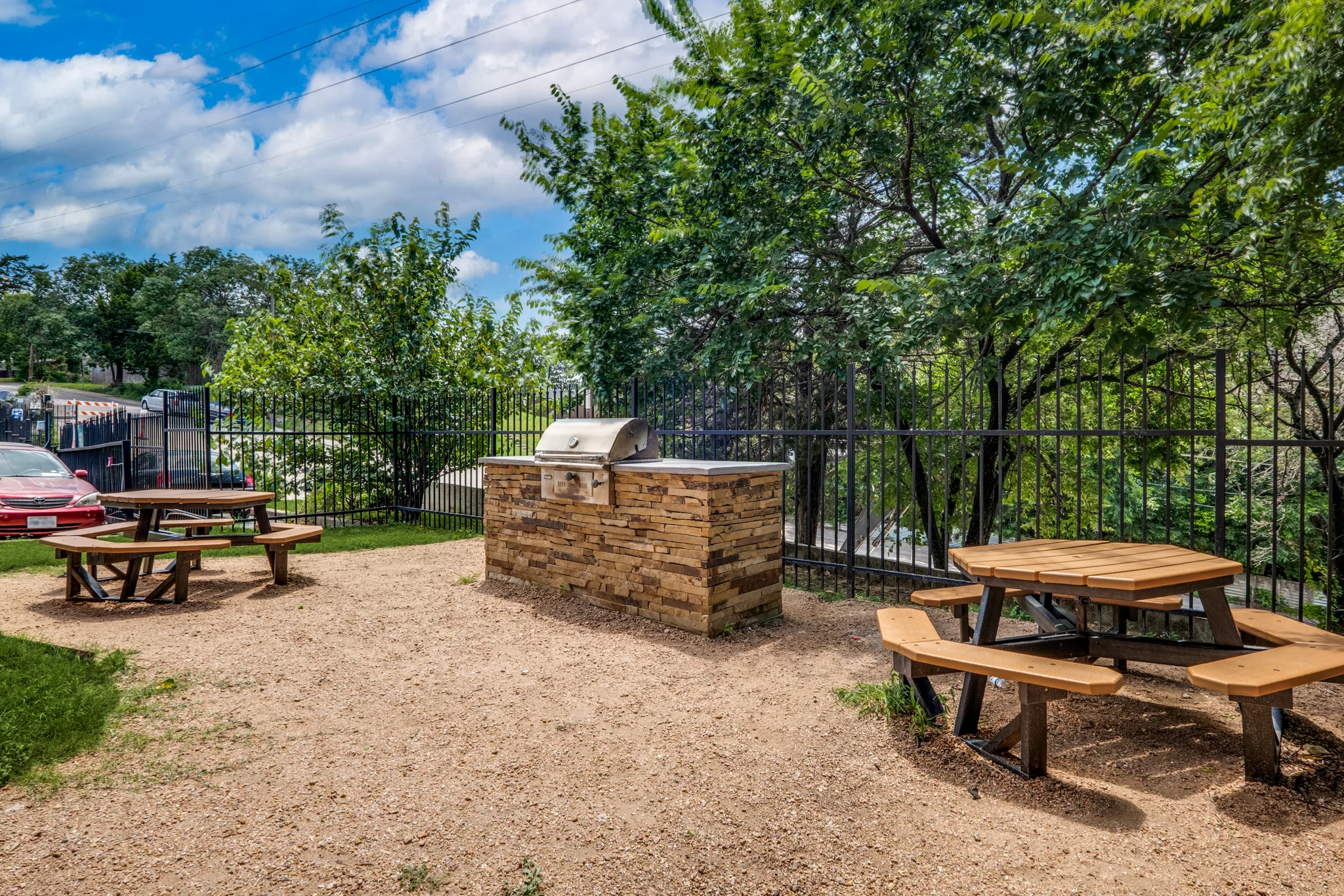 The built in grill station and wooden picnic tables, under the trees behind the fence.