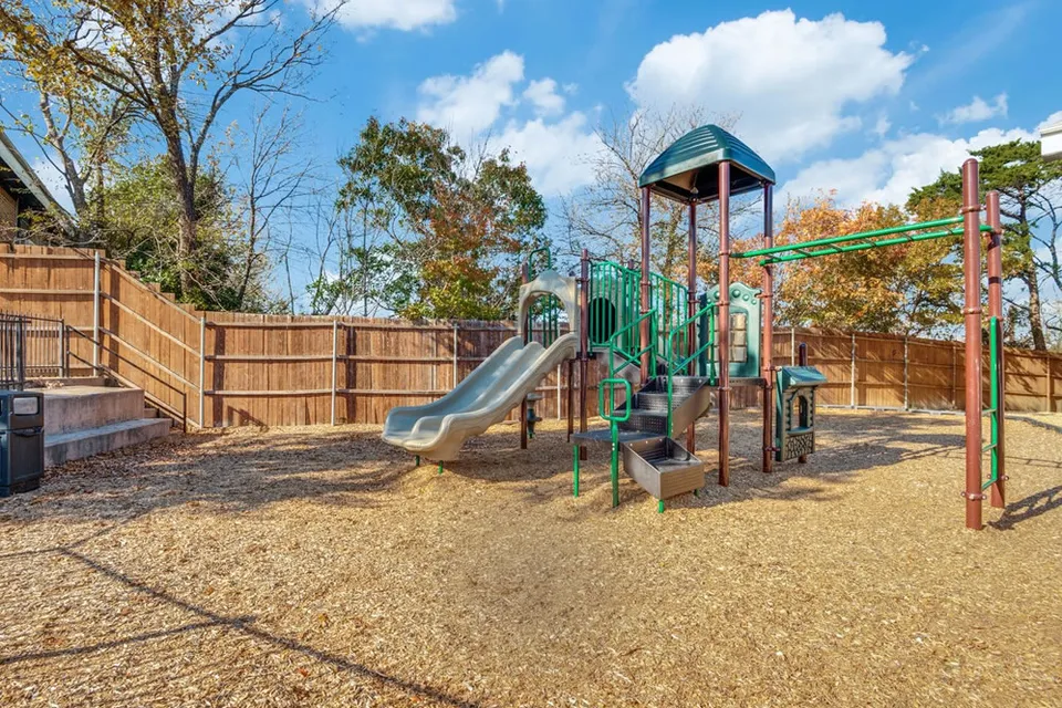 The fenced playground, a slide tower and a climbing frame on wood chips.