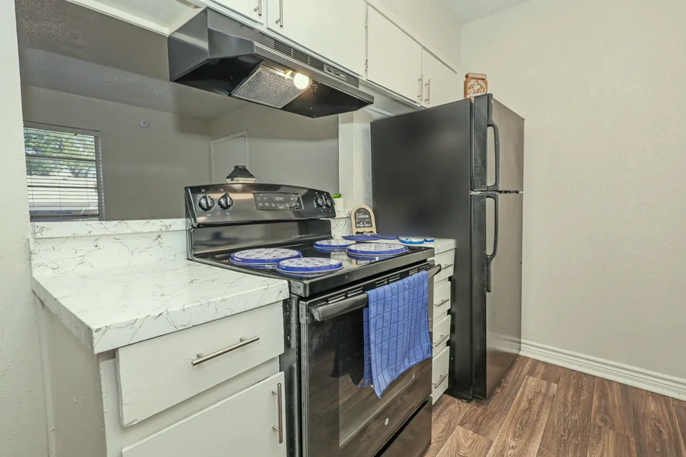 A kitchen with a black range, white cabinets and a marble look quartz counter.