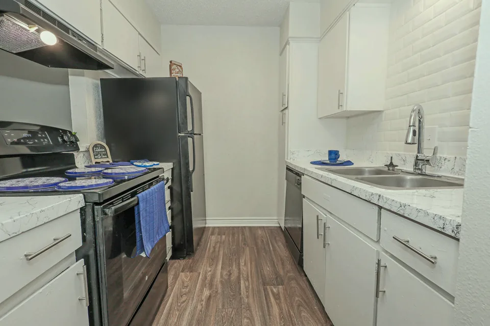 A galley kitchen in white cabinets and white subway tile, sink under the window wall.