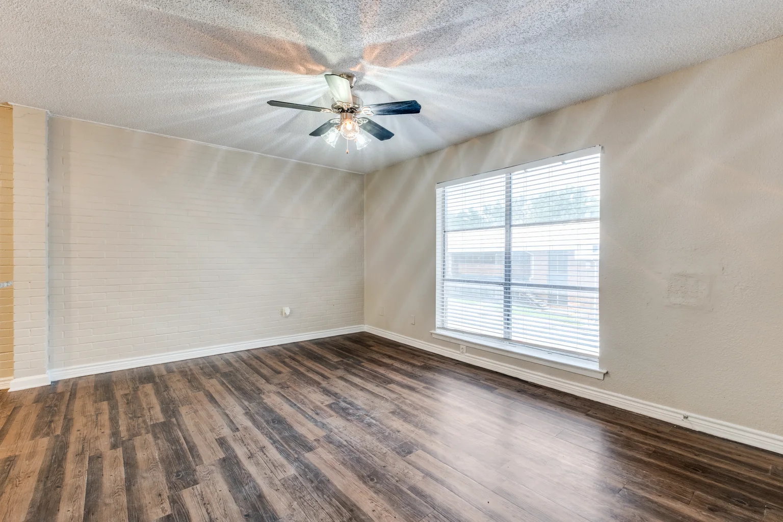 An empty room with a whitewashed brick wall along one side and a window at the end.