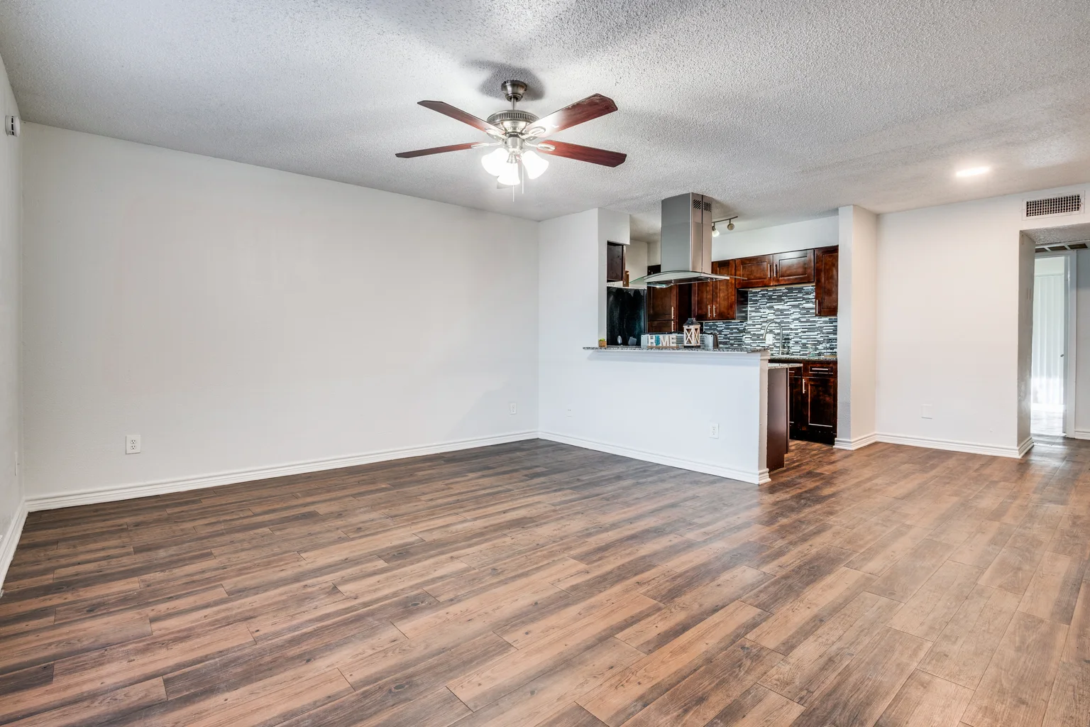 An open living room looking through to a kitchen with dark cherry cabinets.