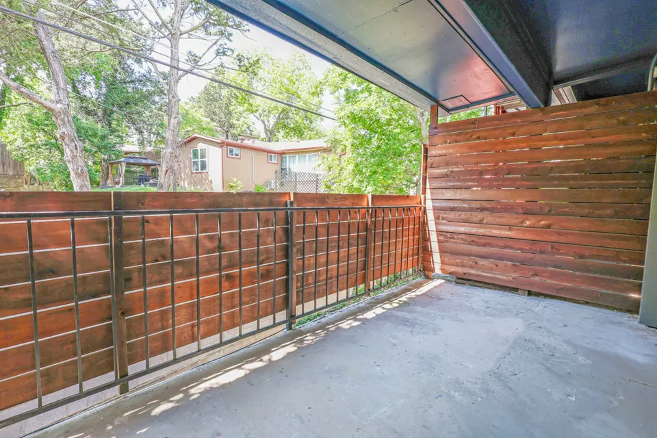 A private covered patio behind a stained wood privacy wall, looking out into the trees.