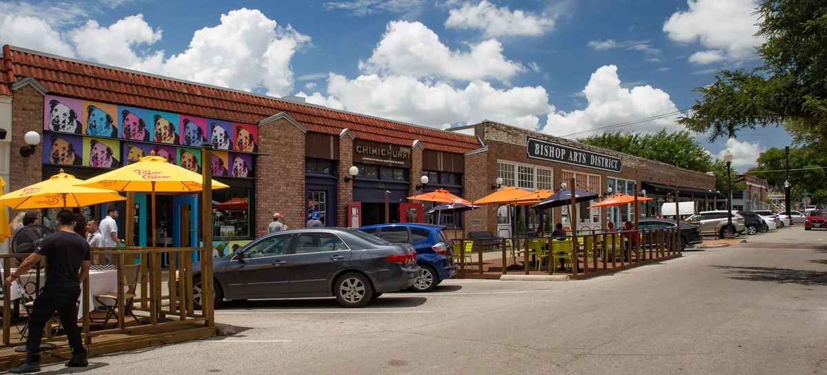 Storefronts and pavement tables under umbrellas along a Bishop Arts District street.